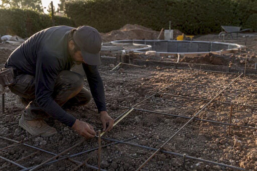 Worker marking steel reinforcement at pool excavation